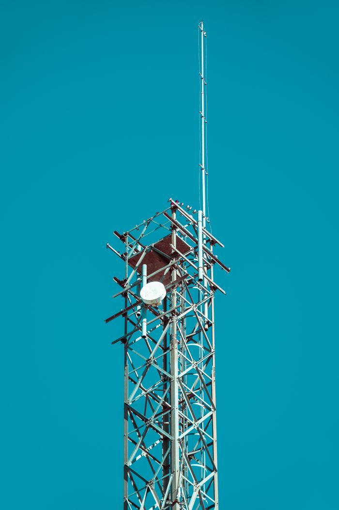 services-04 A metal communication tower with antennas set against a vivid blue sky.