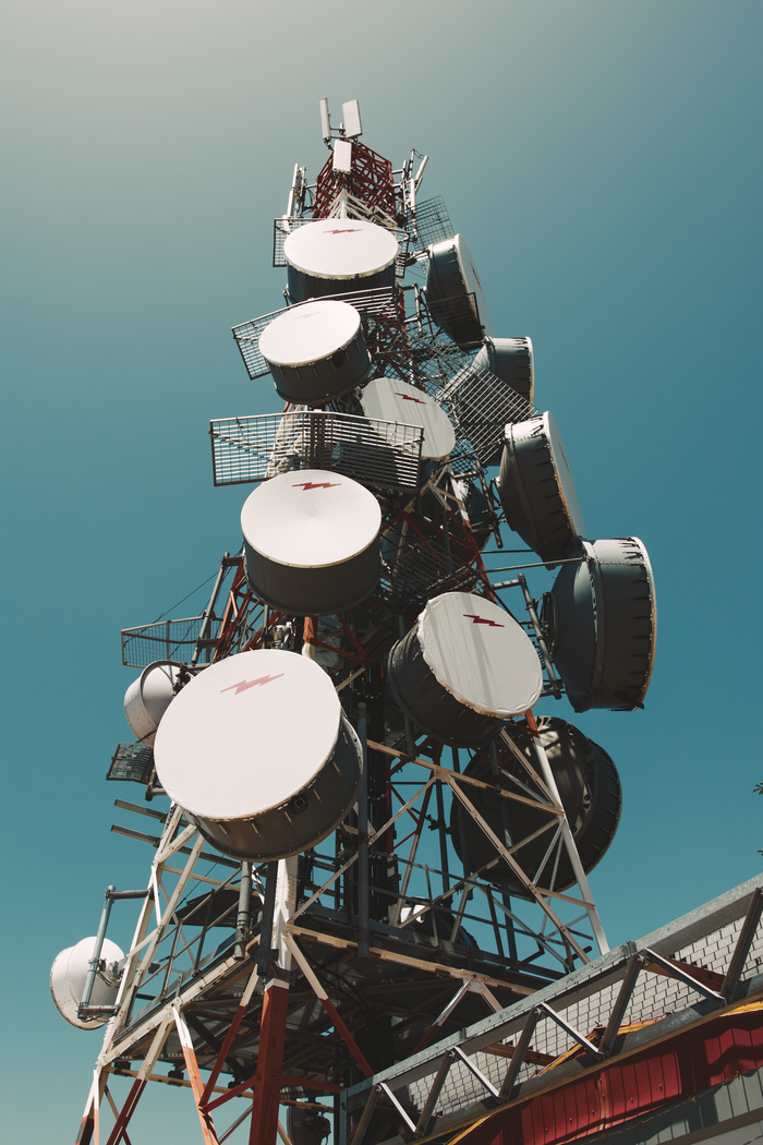 about-img A towering communication tower with satellite dishes under a clear blue sky, symbolizing telecommunications.