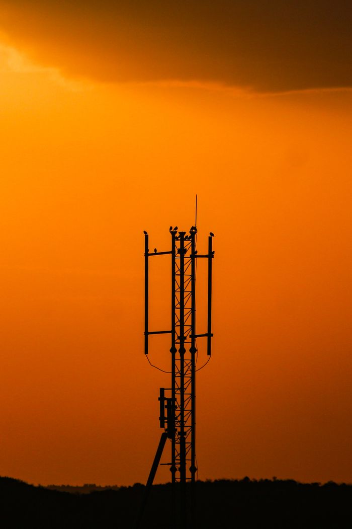 our-experience A striking silhouette of a cell tower against a vibrant orange sunset sky.